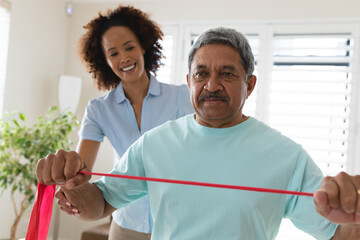 Mixed race female physiotherapist helping senior man exercise using exercise band