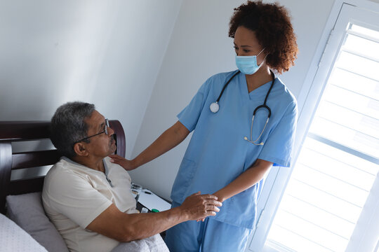 Mixed race female doctor wearing mask ralking with senior man at home