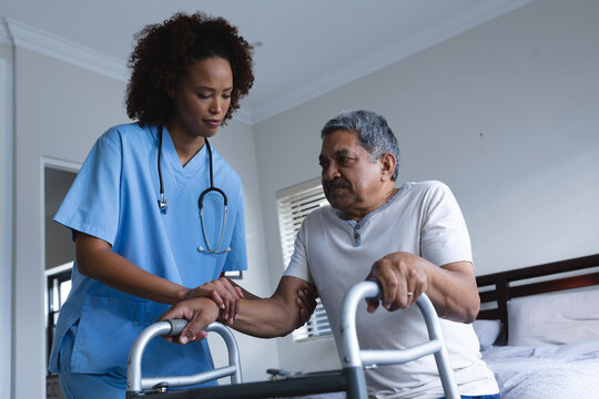 Mixed race female doctor home visiting helping senior man getting out of bed
