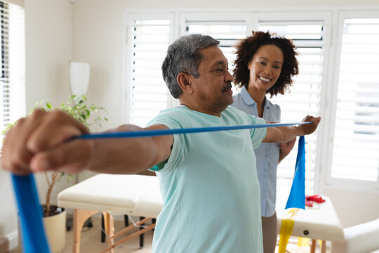 Mixed race female physiotherapist helping senior man exercise using exercise band