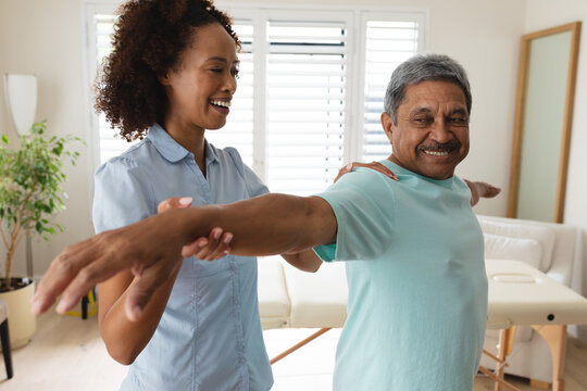 Mixed race female physiotherapist helping senior man stretching his arm