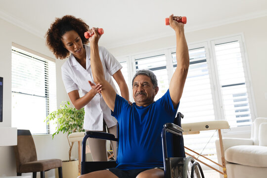 Mixed race female physiotherapist helping senior man exercise using dumbbells