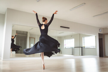 Caucasian female ballet dancer wearing a black dress and focusing on her exercise in a bright studio