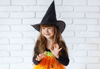 Funny Little Girl In A Witch Costume For Halloween. Happy Halloween! Cute smiling little girl in a pumpkin costume. Girl child witch scares people.The concept of a happy Halloween, masquerade or party