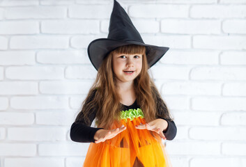 Funny Little 4-year-old Girl In A Witch Costume For Halloween. A pretty smiling little girl in a pumpkin costume. The witch girl scares people.The concept of a happy Halloween, masquerade or party