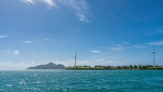 There are wind turbines on an island in the ocean. Turquoise water sparkles in the sun. Light clouds in the blue sky. Copy space. Seychelles © Вера 