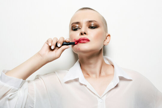 strange woman with short haircut. bald girl smearing red lipstick on her face