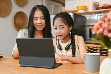Happy Asian family, Mom helping daughter using tablet for studying online classes at home,...