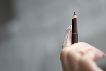 A woman's hand holds a brown makeup pencil.