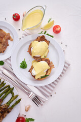 Tasty eggs Benedict, hollandaise sauce and aspargus covered with bacon