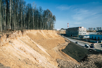 sand pit in the urban landscape. forest on the edge of a slope and and an industrial building in the distance. sand mining for the construction of new buildings