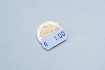 Two euro coin with one euro price tag. Selective focus on label. Inflation in Europe, hyper inflation, devaluation of fiat money concept. - obrazy, fototapety, plakaty
