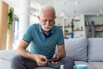 Mature man testing for high blood sugar. Man holding device for measuring blood sugar, doing blood sugar test. Senioir man checking blood sugar level by glucometer and test stripe at home