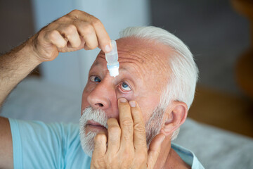 Man putting liquid drops in his eye solving vision problem.Senior dropping eye drop medicine...