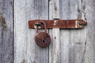 Rusty padlock on the old wooden door of the house, barn. Old hanging metal door lock on a wooden background.