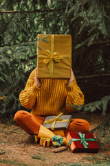 Stylish woman in yellow sweater with Christmas gifts sits near spruce tree