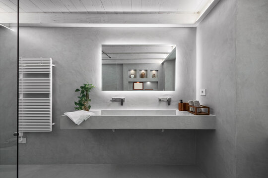 interior view of a modern bathroom covered in grey resin, in the foreground is the built-in washbasin cabinet with built-in washbasin, above it there is a large mirror