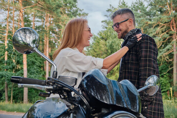 Plakat Middle age couple talking and having fun, sitting on a motorcycle, traveling together on a forest road