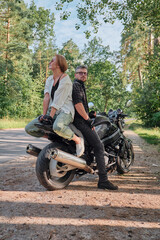 Fototapeta na wymiar Middle age couple talking and having fun, sitting on a motorcycle, traveling together on a forest road