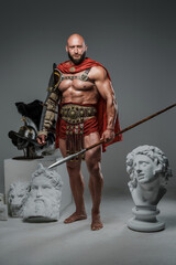Fototapeta na wymiar Portrait of handsome gladiator with spear posing around marble greek statues.