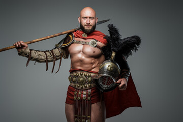 Shot of antique roman warrior with muscular build holding helmet and spear.