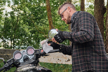 Man biker middle-aged motorcyclist cleaning a motorcycle on the side of the road in the forest