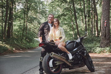 Young beautiful couple hugging, sitting on a motorcycle, travel together on a forest road