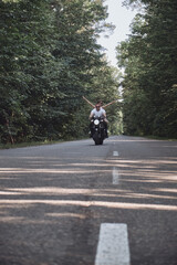 A young happy couple rides a motorcycle on an asphalt road in the forest, freedom and speed