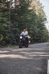 Obraz premium A young happy couple rides a motorcycle on an asphalt road in the forest, freedom and speed