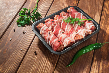 Raw meat Lula kebab wrapped in bacon in a plate on a vintage table with spices and pepper. Free space for advertising.