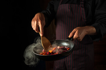 Cooking vegetables on a hot frying pan in the hands of a chef. Molecular gastronomy or cuisine