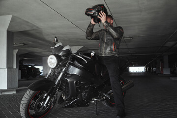 A man sitting on a motorcycle takes off his helmet in underground parking garage, in motion
