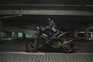 Plakat Young woman biker in a helmet sitting on a motorcycle in the underground parking garage