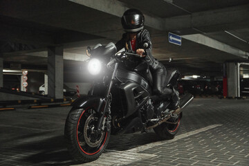 Obraz na płótnie Canvas Young woman biker in a helmet sitting on a motorcycle in the underground parking garage