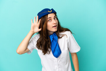 Fototapeta premium Airplane stewardess woman isolated on blue background listening to something by putting hand on the ear