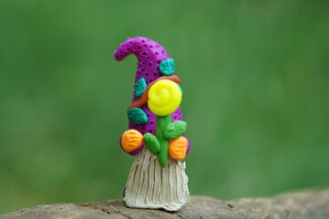 A small toy gnome with a flower on a green background. Fabulous scenery.