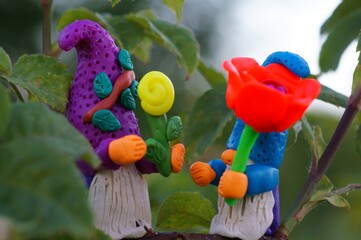 Figures of dwarfs with flowers on a tree branch. Fabulous toys made of plasticine.