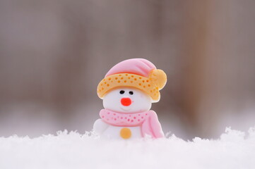 A toy little snowman decorated with a scarf on a snow background. Christmas toys.