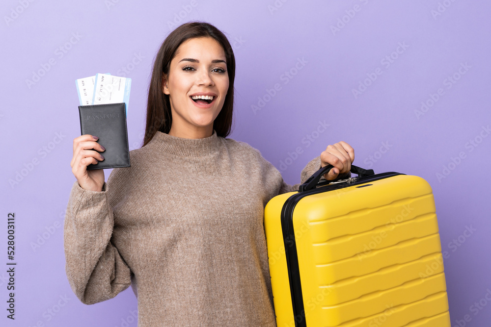 Wall mural Young caucasian woman isolated on purple background in vacation with suitcase and passport