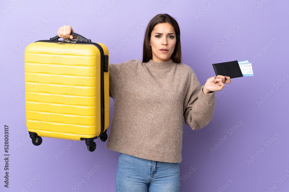 Sticker Young caucasian woman isolated on purple background unhappy in vacation with suitcase and passport