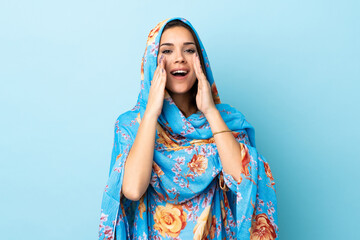 Young Moroccan woman with traditional costume isolated on blue background shouting and announcing...