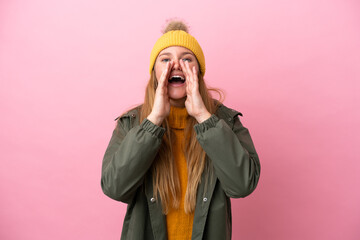 Young blonde woman wearing winter jacket isolated on pink background shouting and announcing something