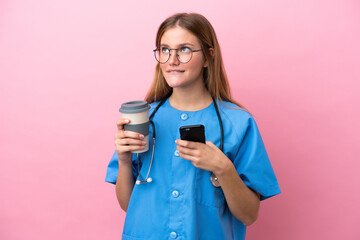 Young surgeon doctor woman isolated on pink background holding coffee to take away and a mobile while thinking something