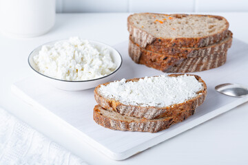 Fototapeta na wymiar Fresh bread with carrots on a white wooden cutting board with curd cheese