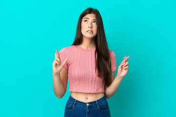 Young Brazilian woman isolated on blue background with fingers crossing and wishing the best