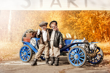 Young happy children. Little funny boys in the form of racers began to play as a team on an old racing car in the autumn park. Art photography of kids in retro style.