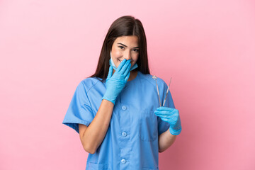 Dentist woman holding tools isolated on pink background happy and smiling covering mouth with hand