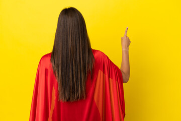 Super Hero Brazilian woman isolated on yellow background pointing back with the index finger