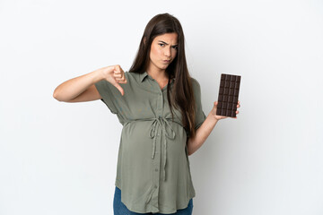 Young Brazilian woman isolated on white background pregnant and holding chocolate doing bad signal