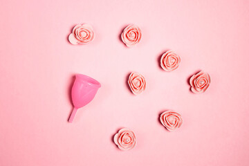 Menstrual cup with rose flowers on a pink background.